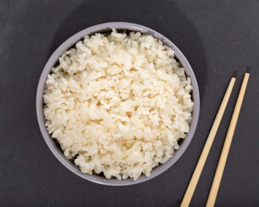 Cooked rice in bowl and chopsticks on black slate. Top view