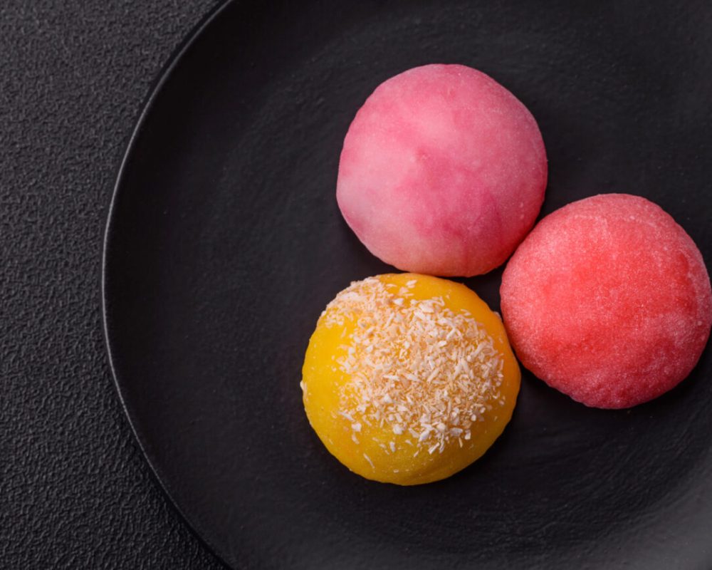 Delicious colorful asian mochi sweets with rice dough shell and fruit filling on dark concrete background